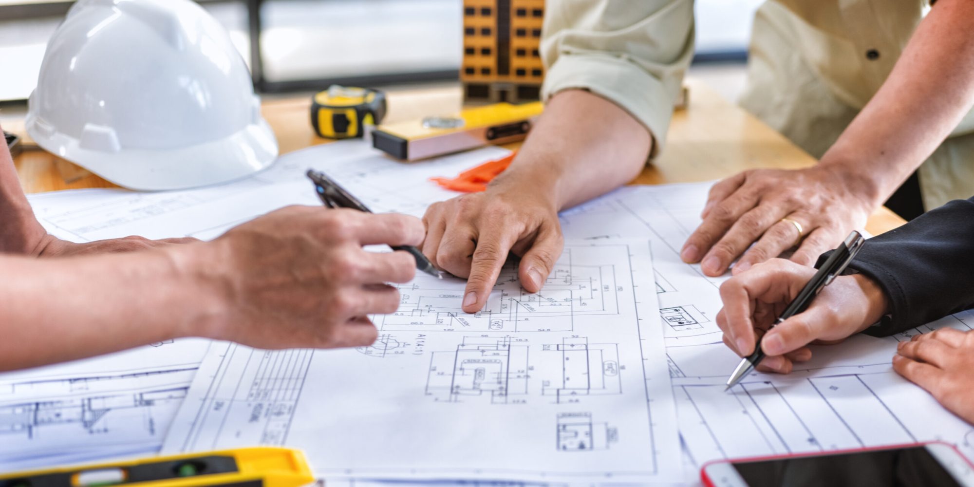 Team engineer meeting for colleagues discussing and checks construction blueprints on new project at desk in office.