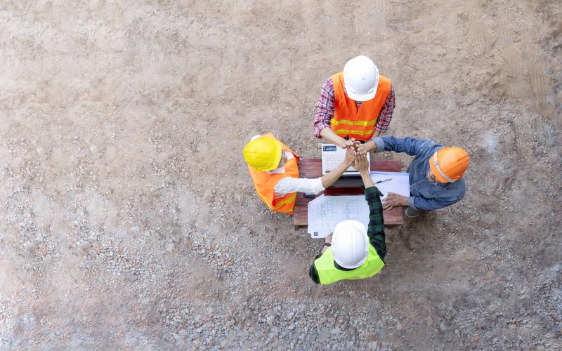 top view of engineering team in uniform meeting on desk with blueprint and laptop on site work,doing hands high five for success of cooperation  in the future